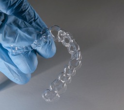 Gloved hand holding clear aligner