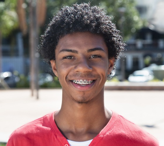 Boy in red shirt smiling outside and showing braces